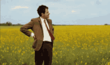 Animated gif of Mr. Bean standing on the side of a road next to a field impatiently checking his watch